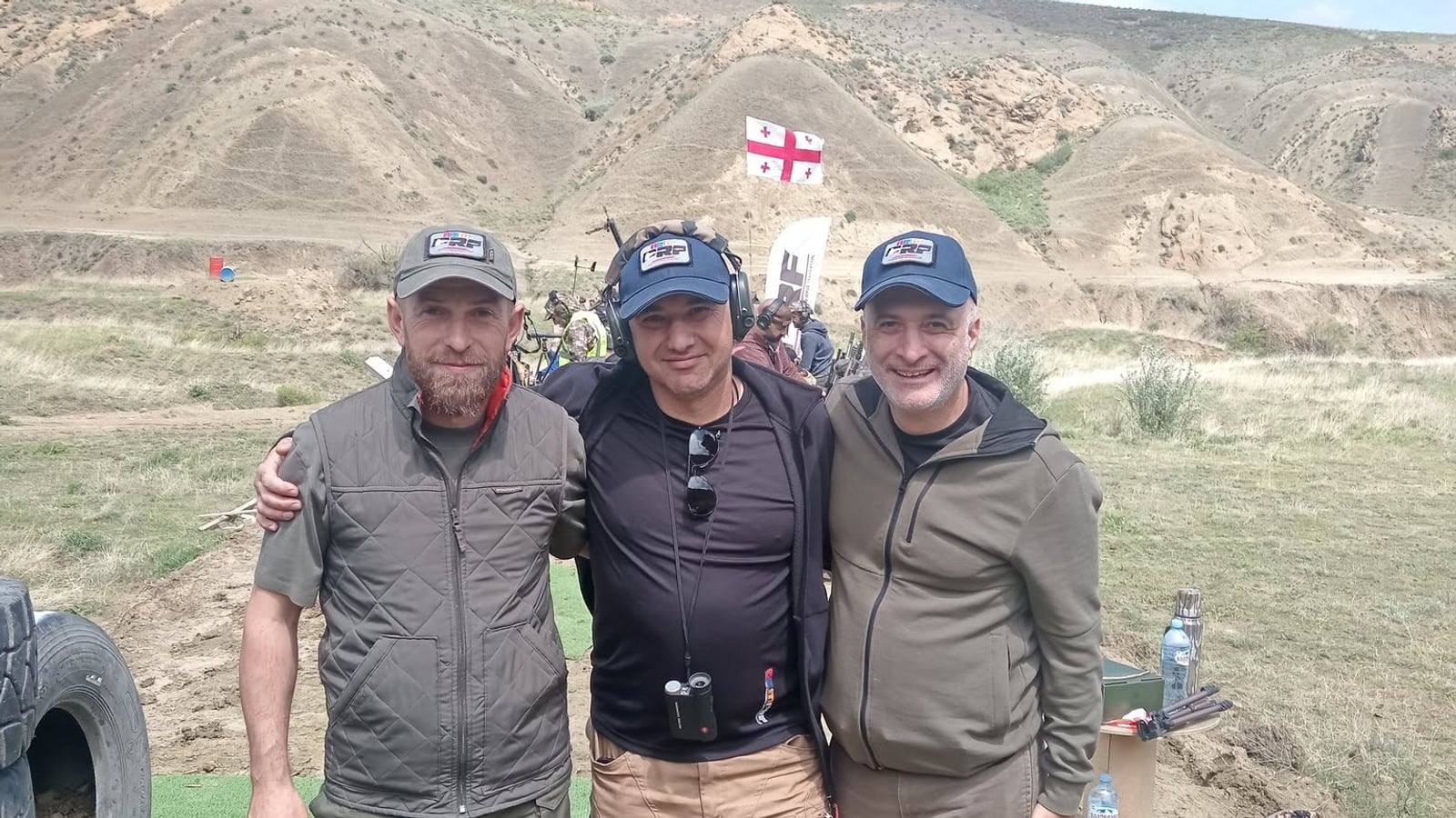 Three ARMPRF representatives at the range, the Georgian flag on the hillside behind