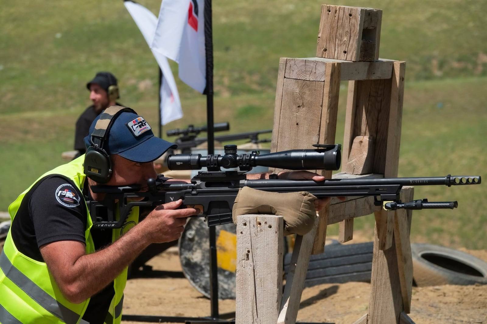 A range officer shooting a positional stage off a wooden prop