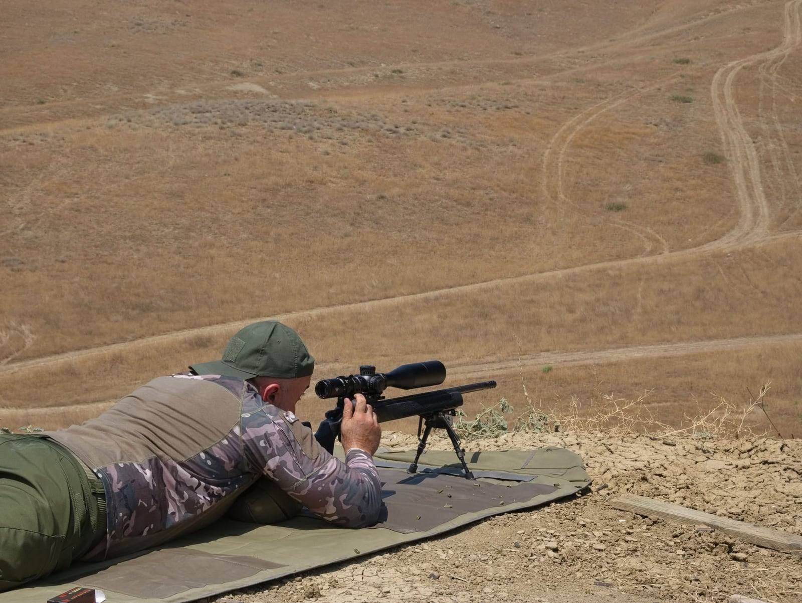 A shooter prone with a .22LR rifle, targets on the slope below