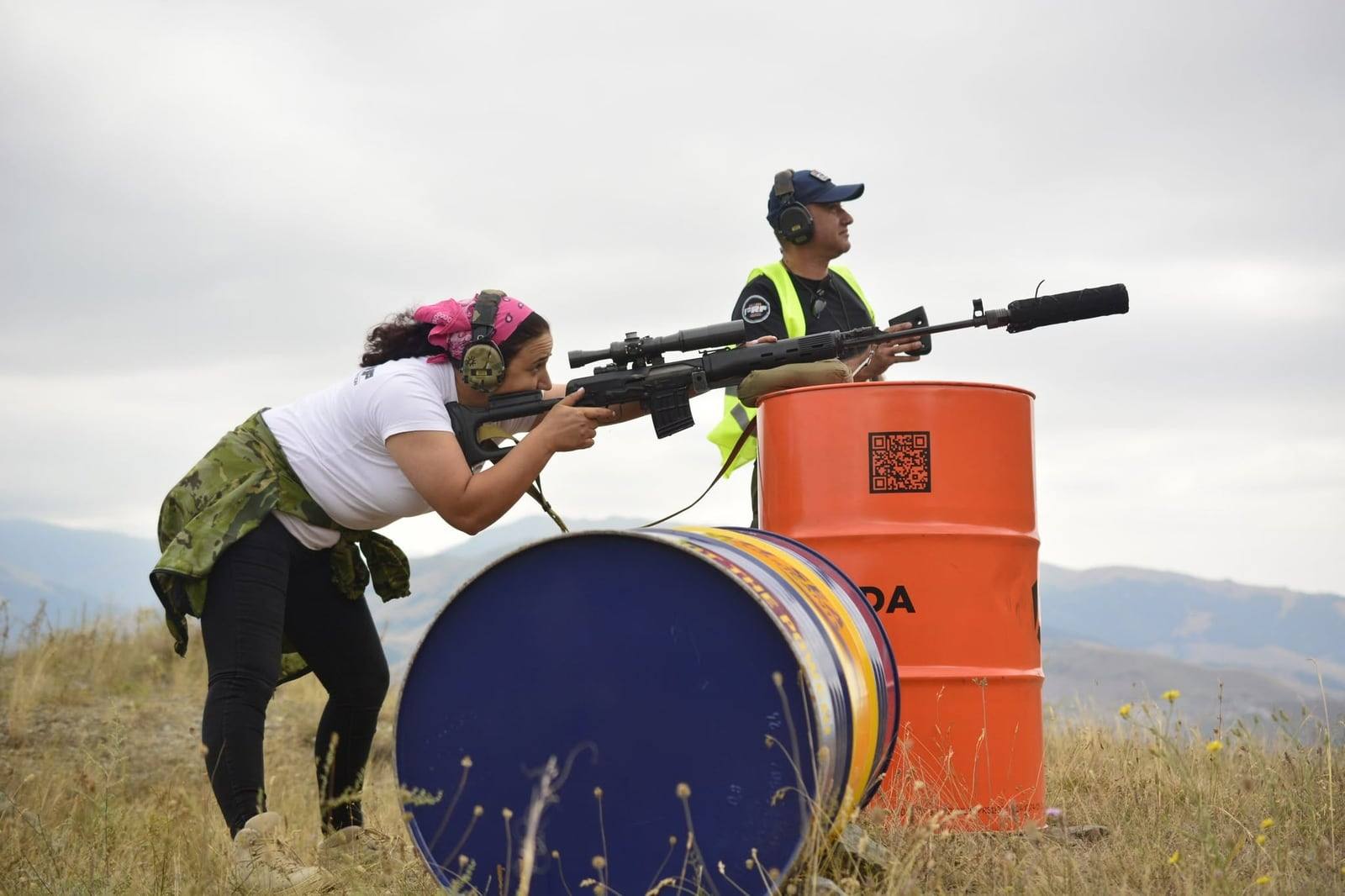 A competitor shooting an SVD off a barrel while the range officer watches