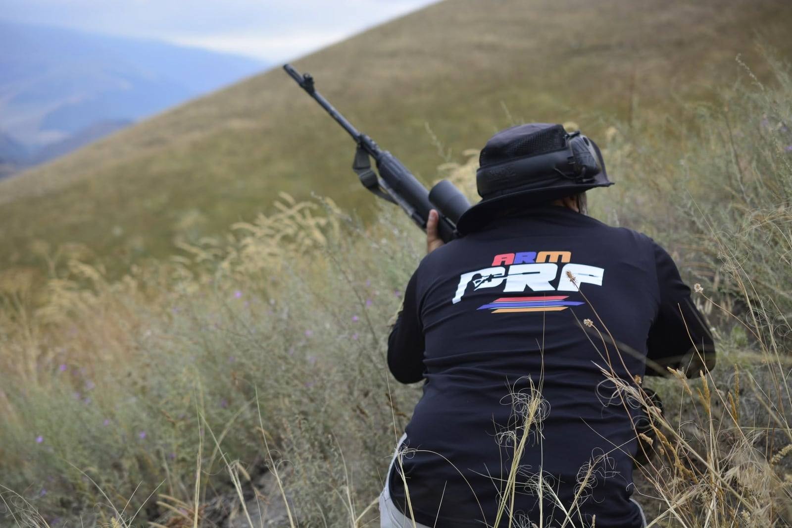 A shooter in an ARMPRF shirt taking position on the hillside