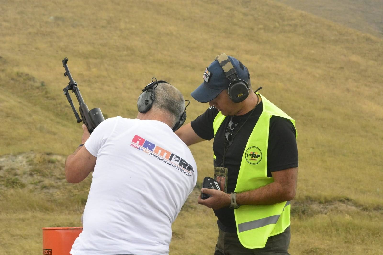 The range officer running the timer beside a shooter on a stage