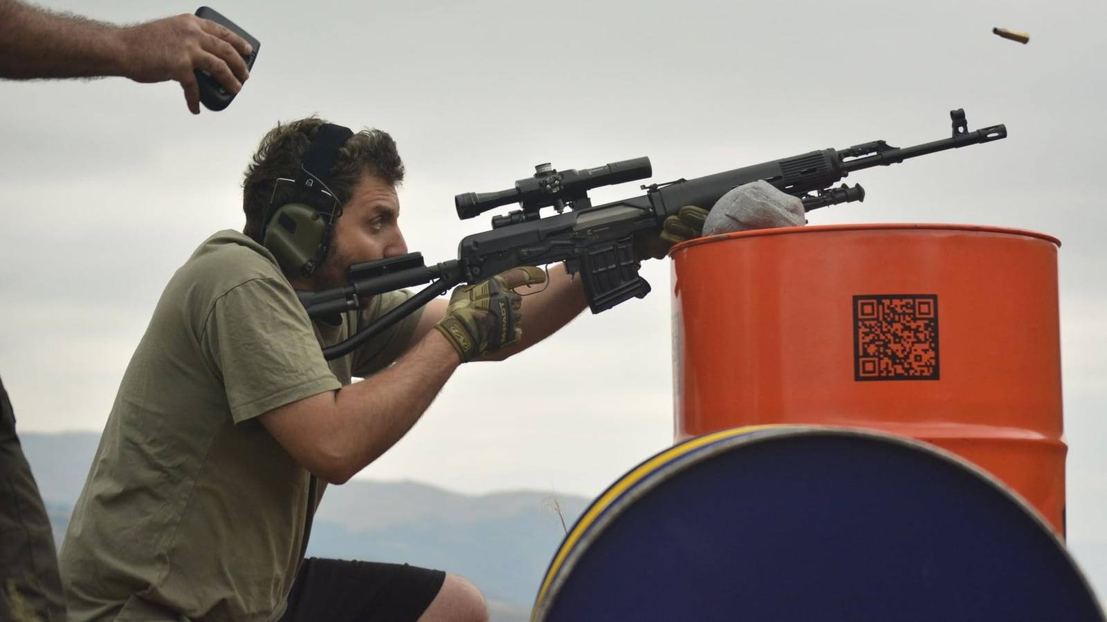 A shooter firing an SVD off a barrel rest, the case still in the air